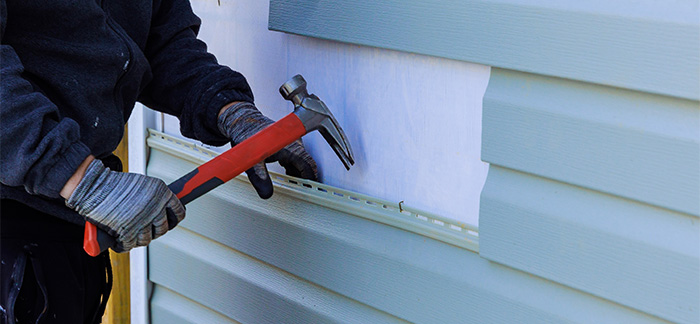A person lifting the vinyl siding of a home.
