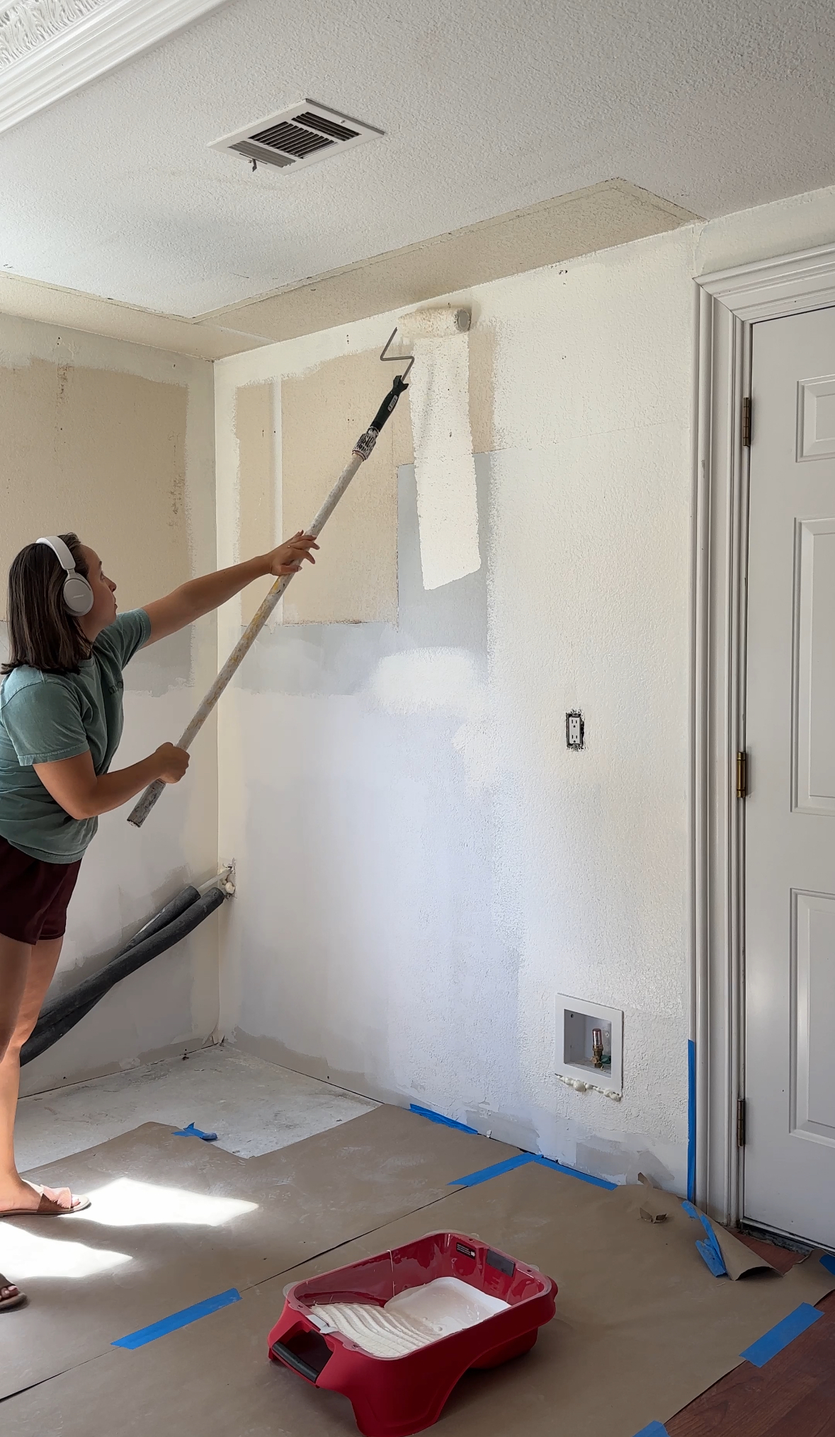 Person wearing headphones painting a white wall with a roller during a kitchen renovation in Antioch, CA.