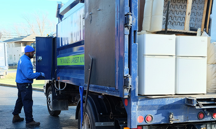 1-800-GOT-JUNK? truck team dropping off appliances, including a mini fridge, at a recycling facility.